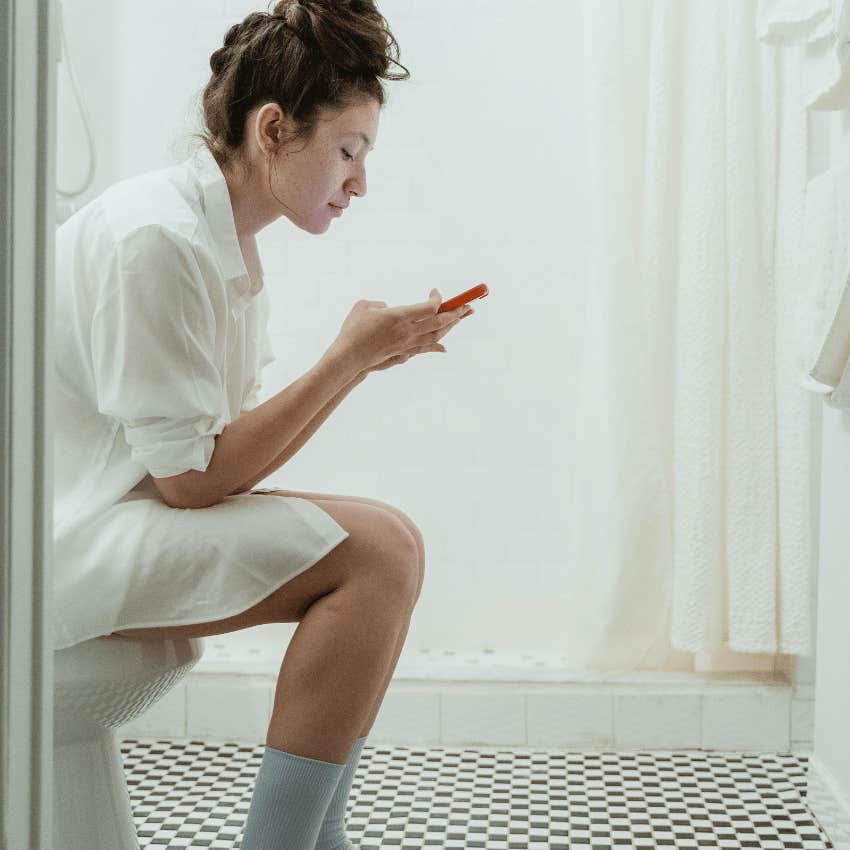 woman using phone while sitting on toilet