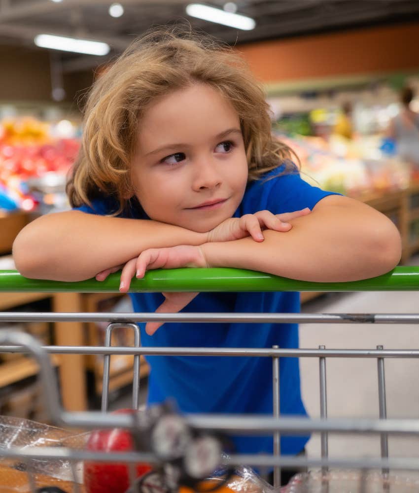 Young boy leaning on shopping cart in grocery store