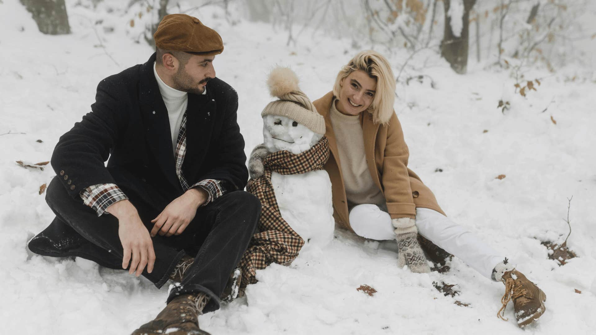 couple sitting next to a snowman they built