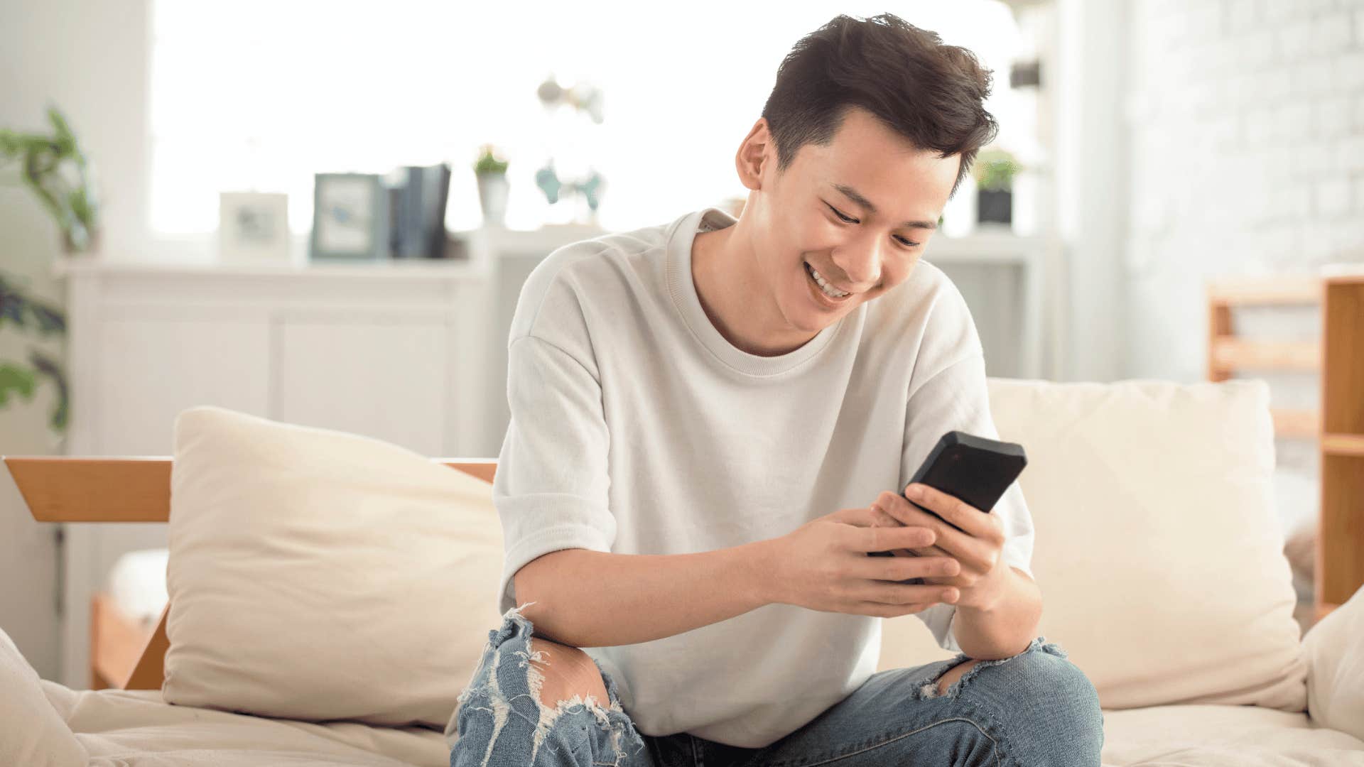 young man on couch smiling down at phone