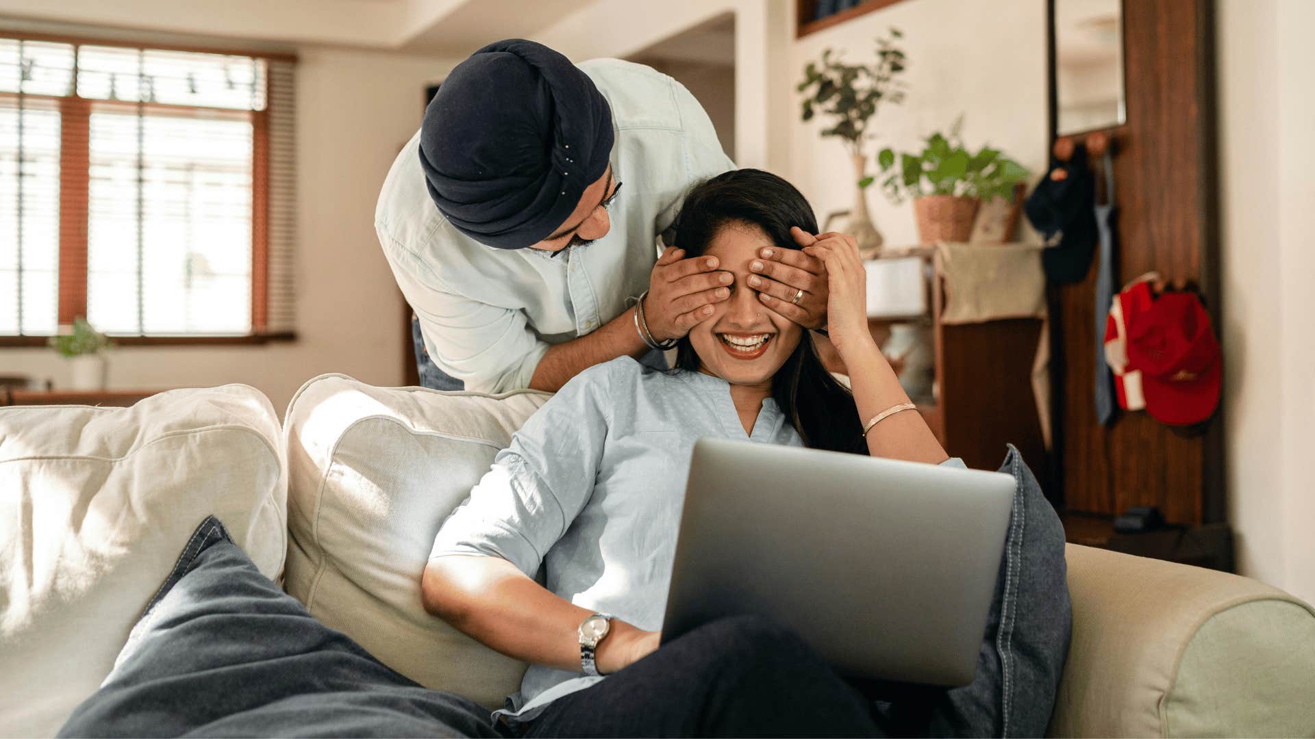 husband surprising wife while working on a laptop