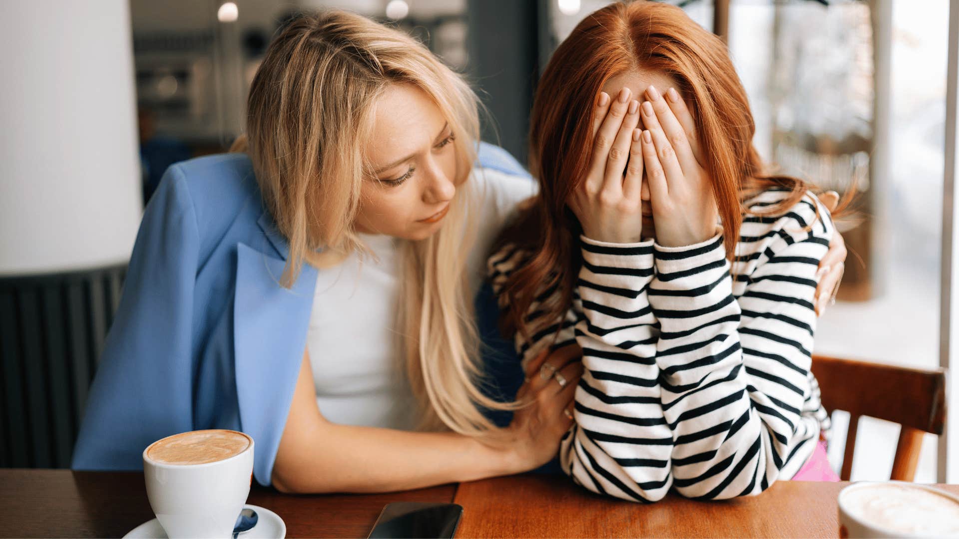 blonde woman comforting redhead woman