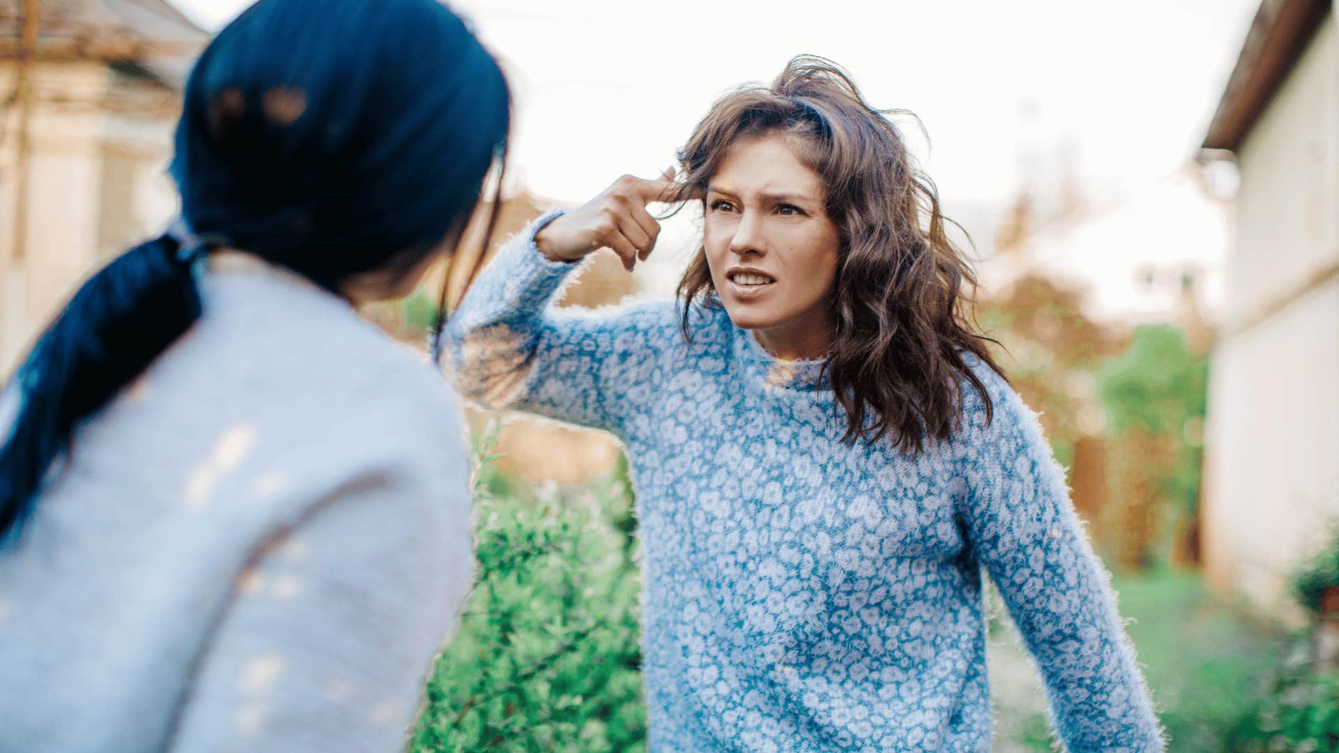 two women arguing outside while one woman points to her head