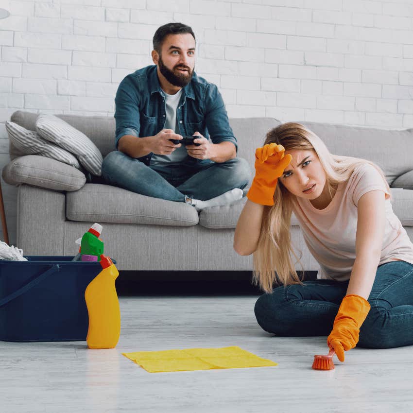 annoyed wife scrubbing floor while husband plays video games