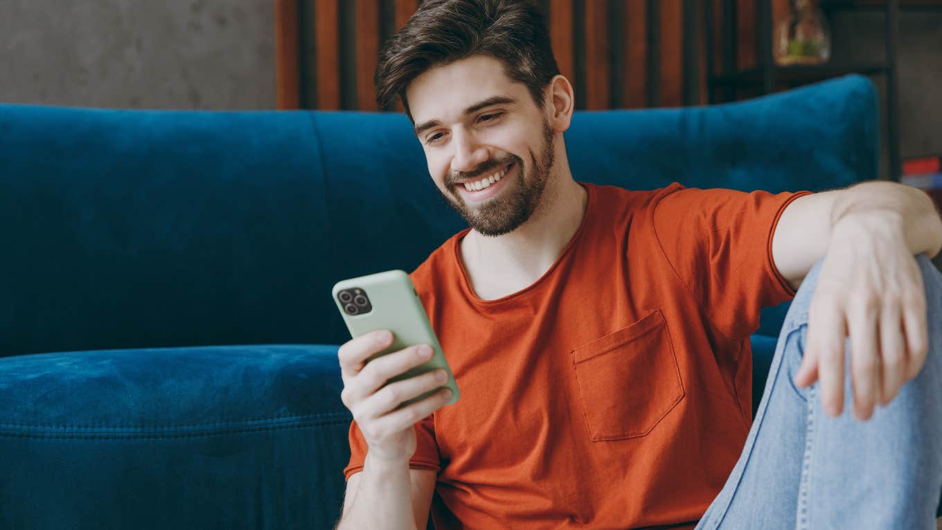 Man smiling while holding his phone on the couch.