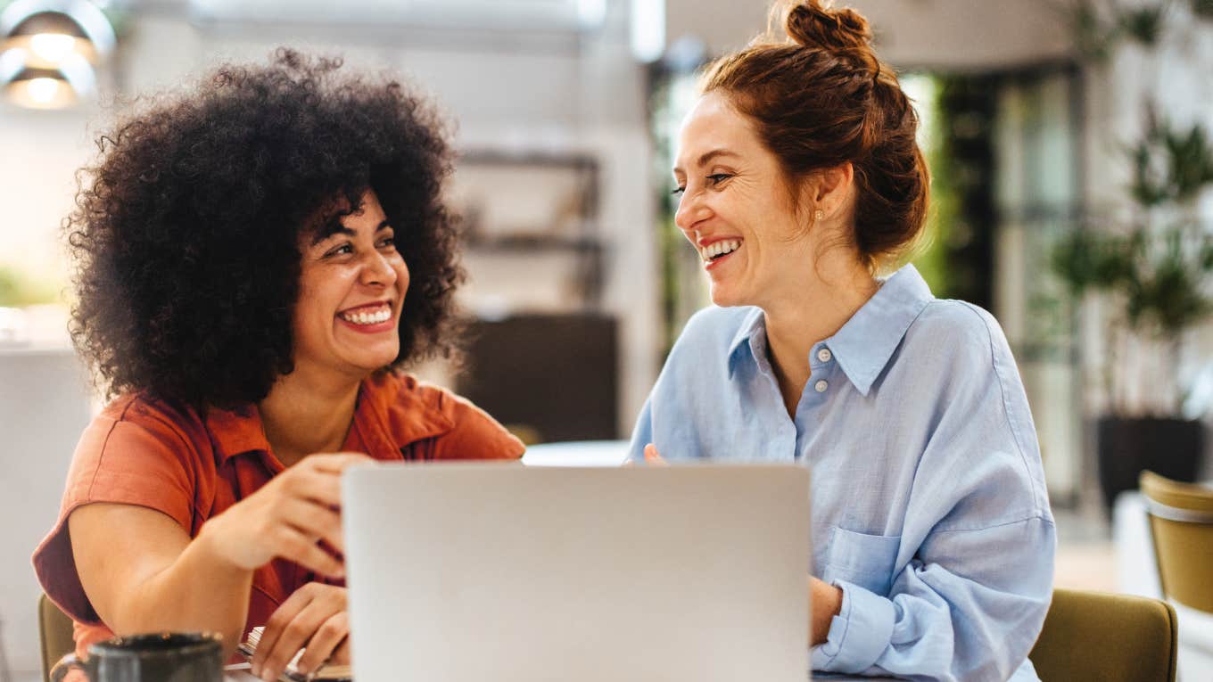 Two women smiling and working together in an office.