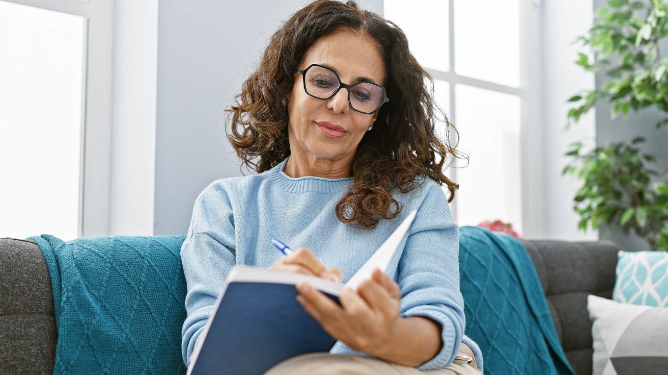 Older woman with glasses writing in a notebook.