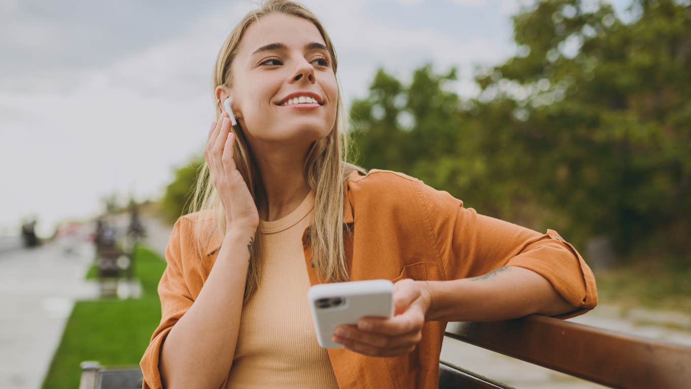 Woman smiling and holding her phone outside.