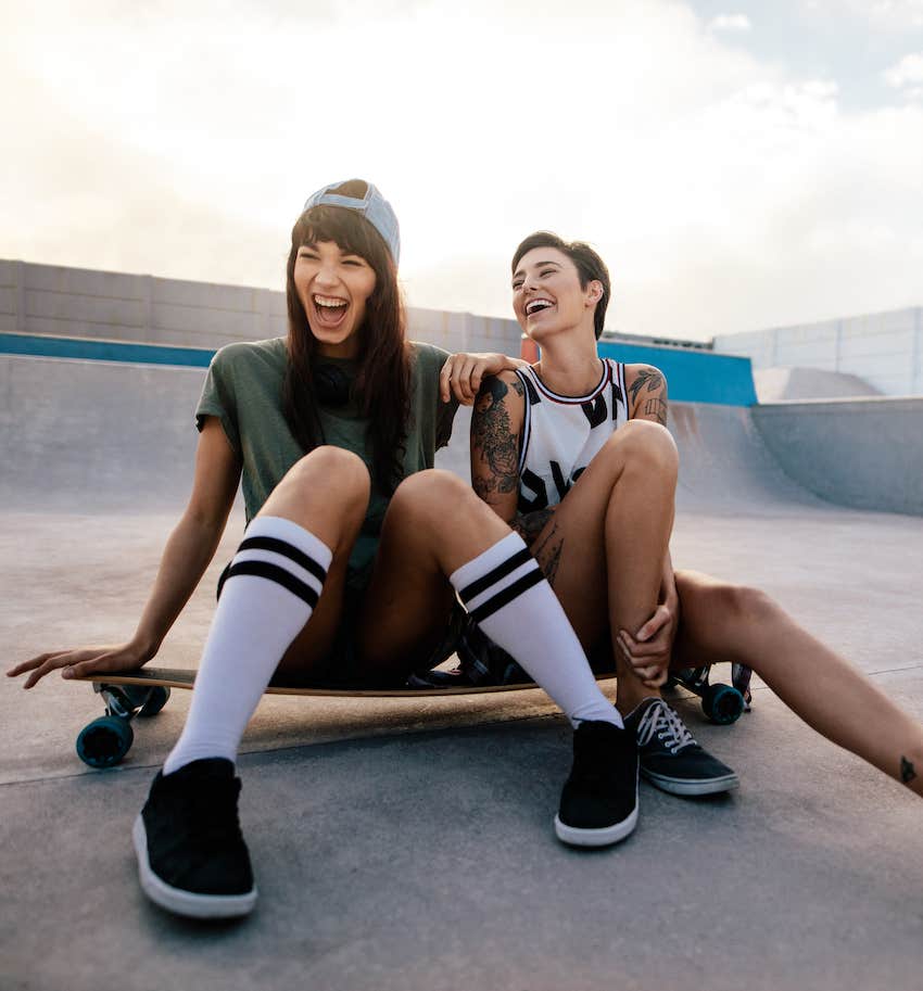 Couple at skate park sit on skate board and laugh