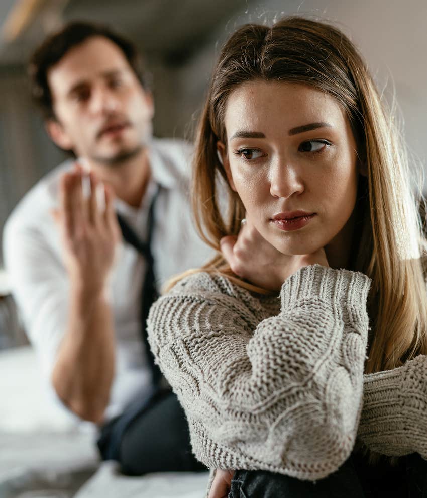 She hold her neck and crosses other arm while he gestures aggressively in the background