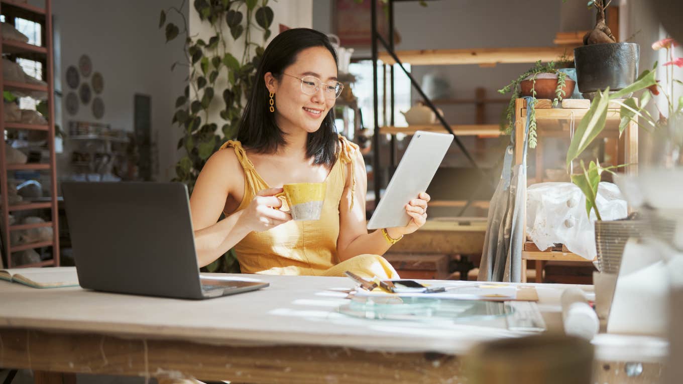 woman sitting at desk on break enjoying coffee reading tablet