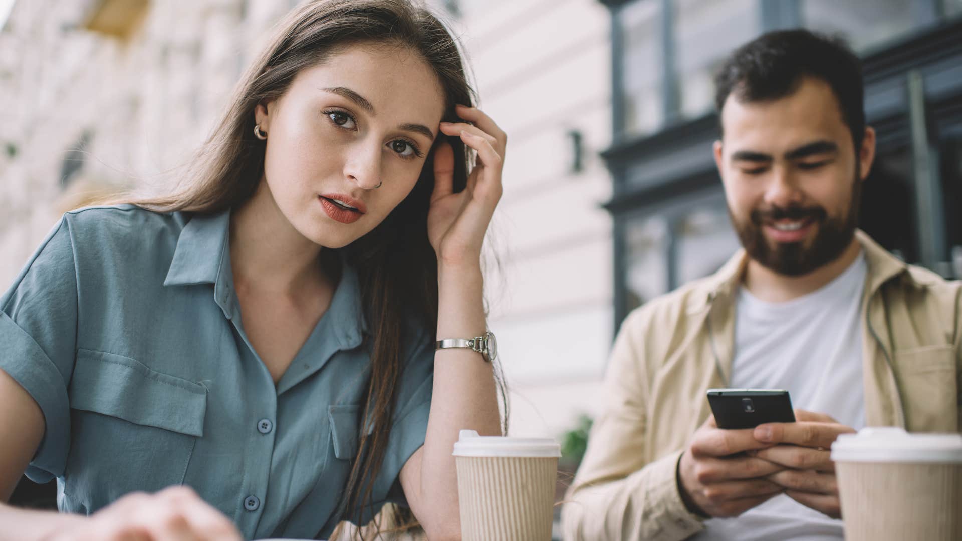 Woman looking at the camera while a man scrolls on his phone next to her.