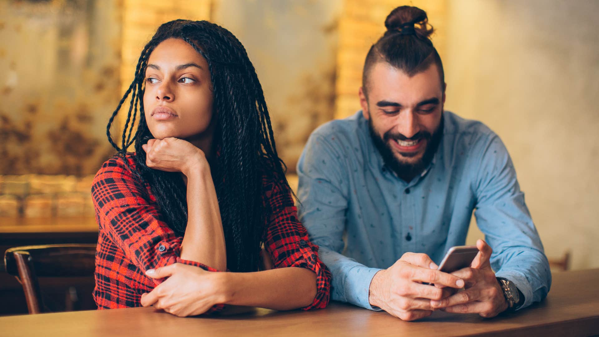 Woman looking away from her partner on his phone.