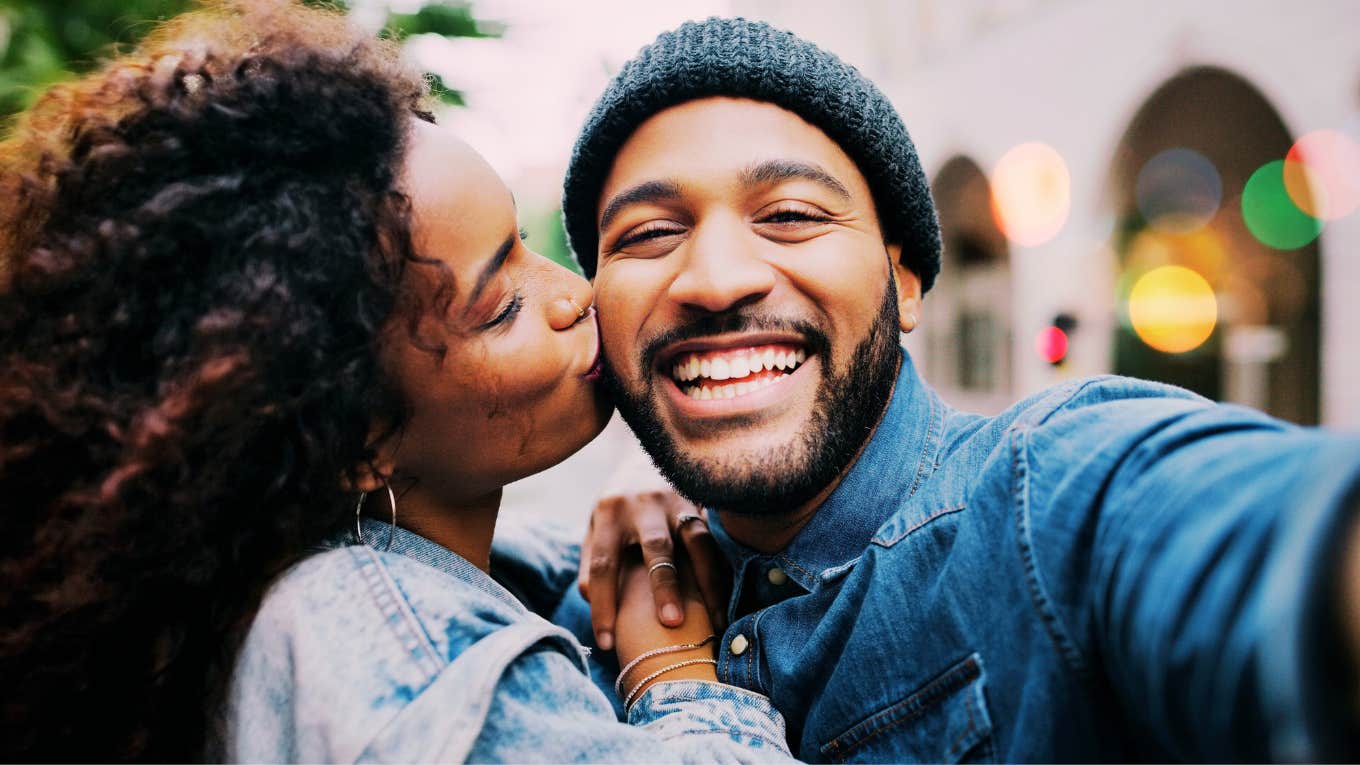 Woman clinging to mans side, embracing a big kiss on the cheek. 