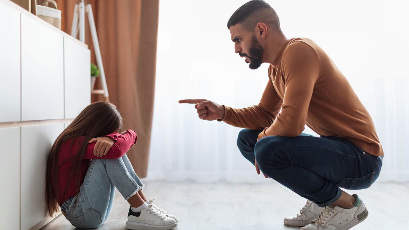 dad crouching down to scold his young daughter who is sitting on floor