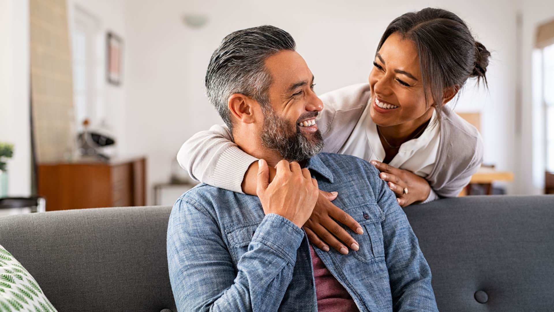 Woman hugging her husband over the couch.