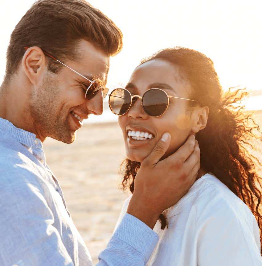 He touches her face silently while walking on the beachj