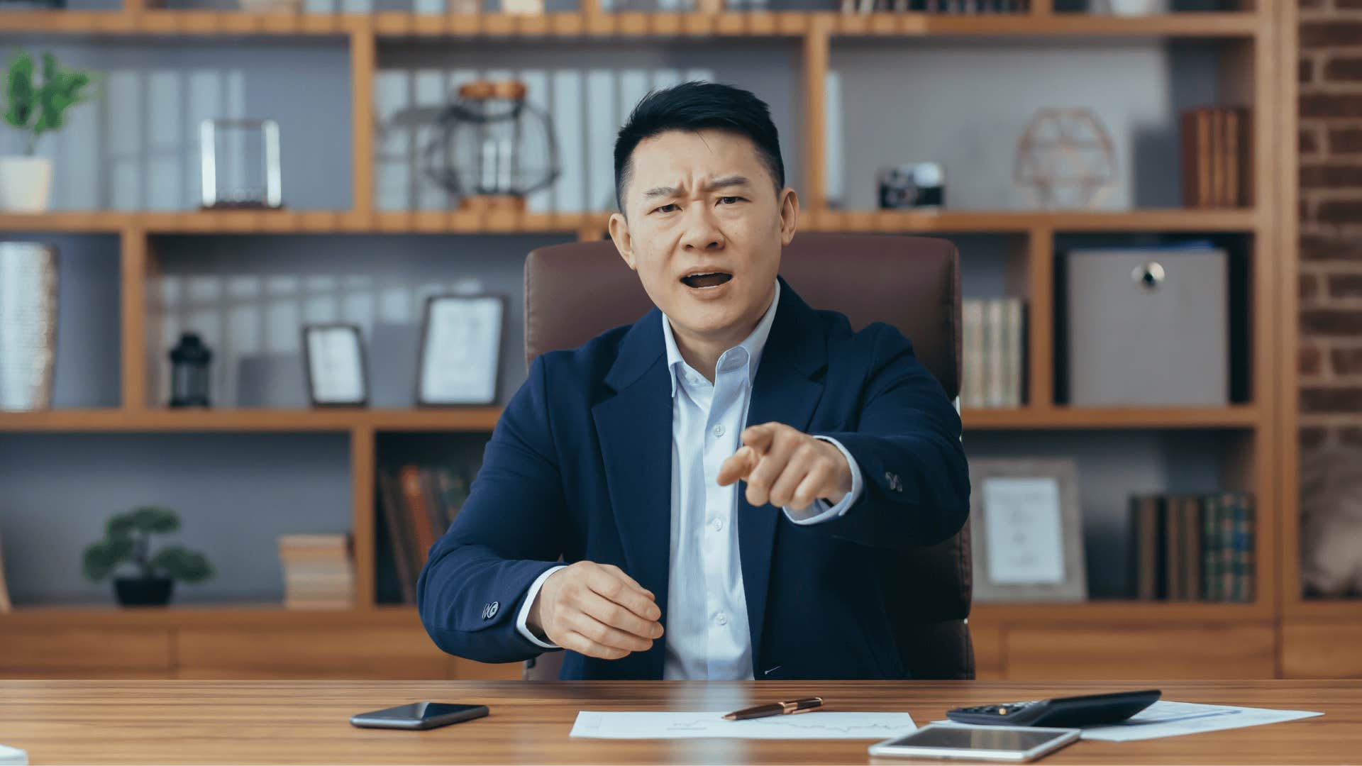 Man sits behind desk, points and shouts 