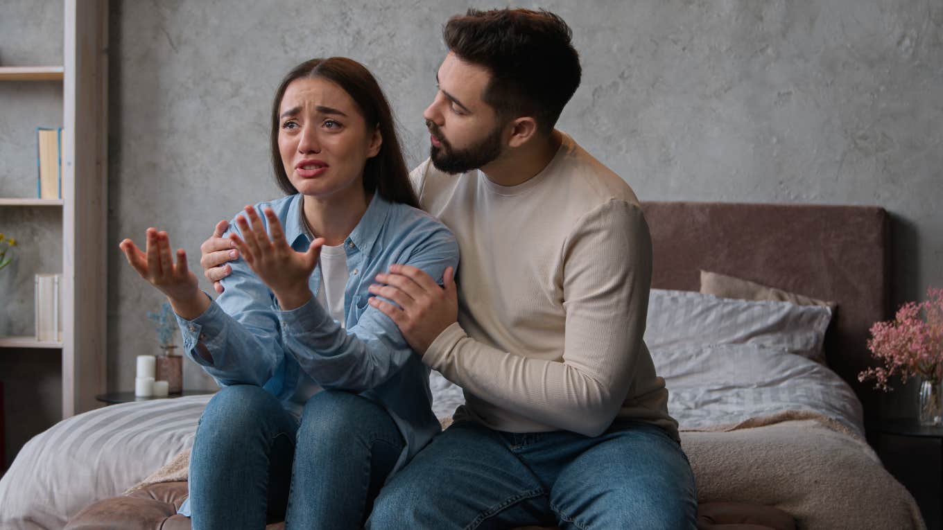 husband trying to calm down crying wife while sitting on bed