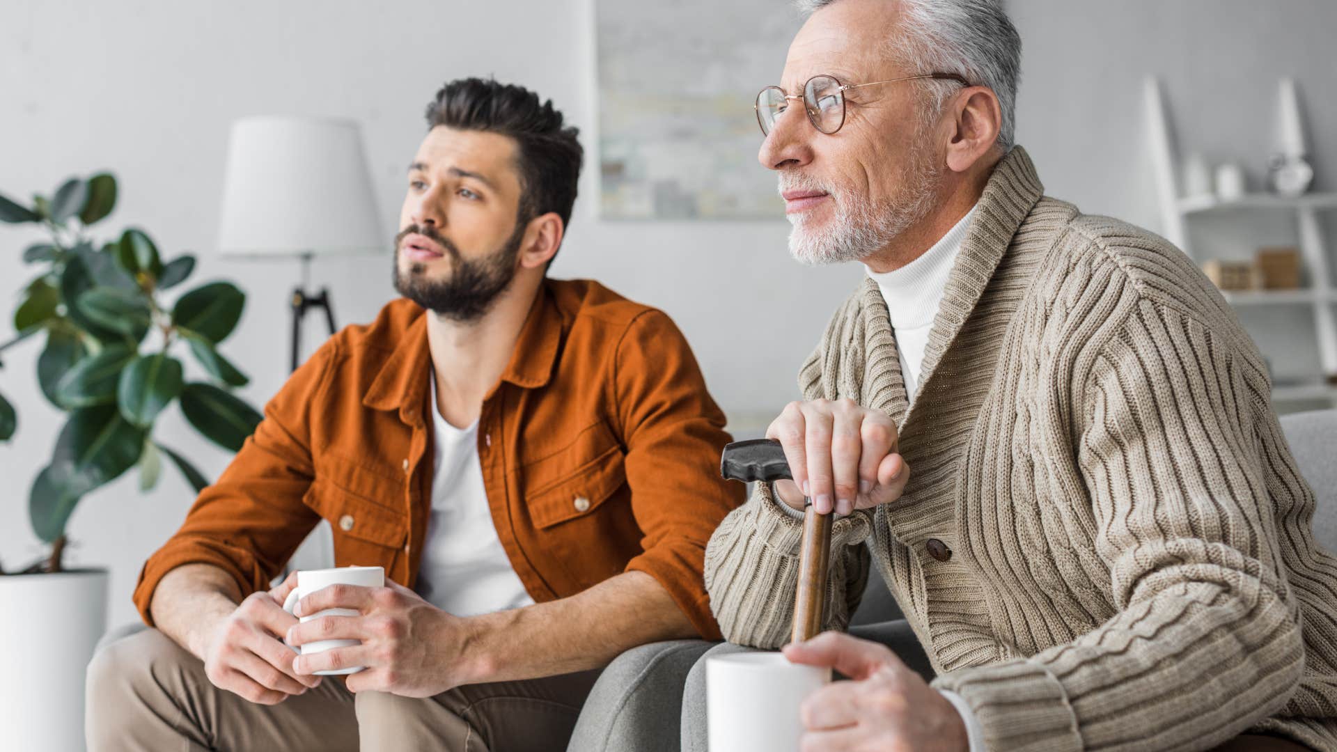 Adult son and father watching television together at home. 