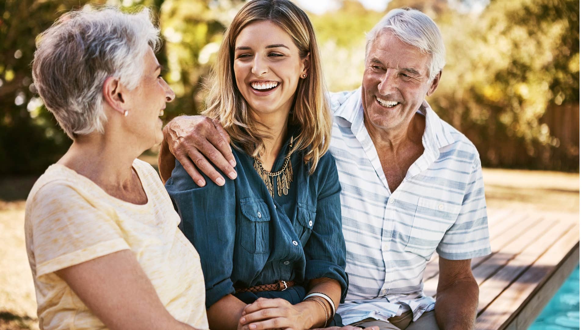 Parents smiling with their adult daughter outside.