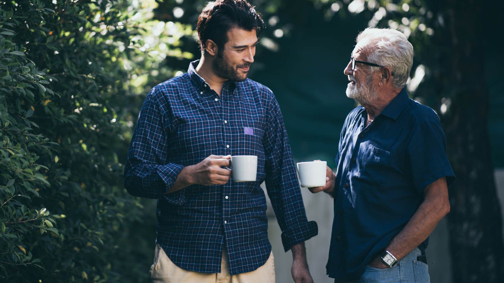 Father and adult son smiling and drinking coffee outside.