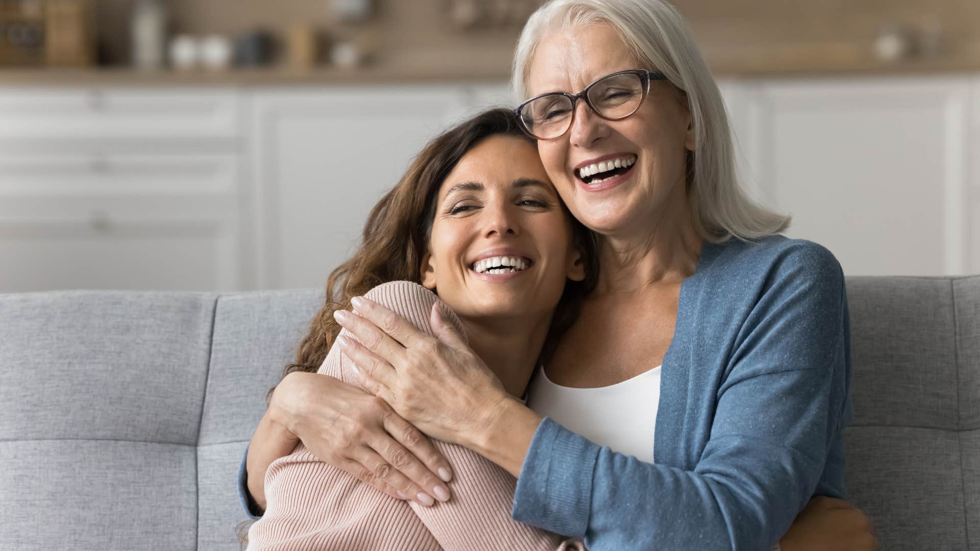 Mother and adult daughter hugging each other and smiling.