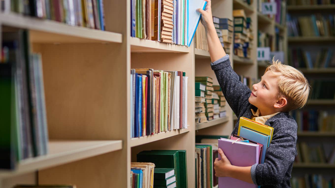 little boy taking books off of library shelves