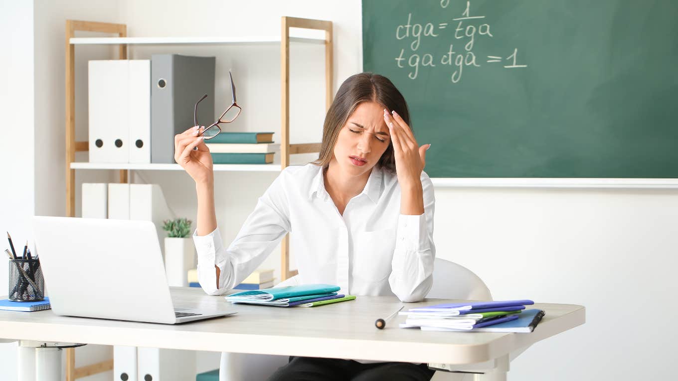 stressed teacher sitting at her desk in front of a blackboard