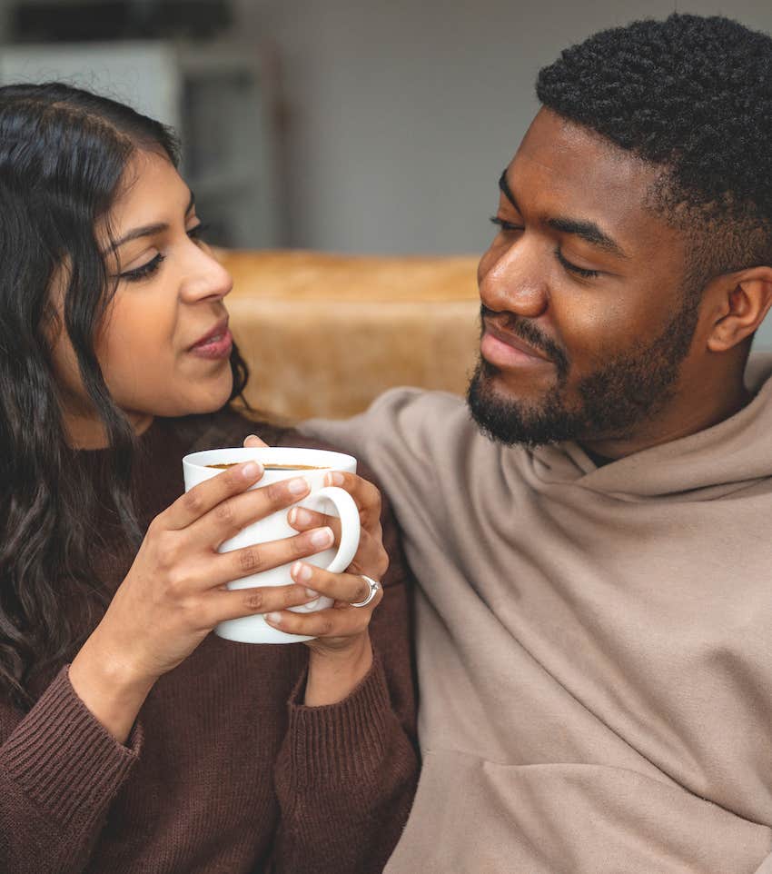 She holds coffee cup and looks at him, both are calm