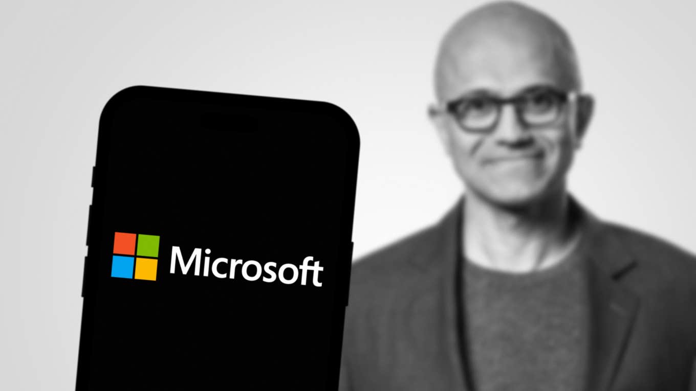 Microsoft logo displayed on smartphone screen with CEO of Microsoft Satya Nadella in the background.