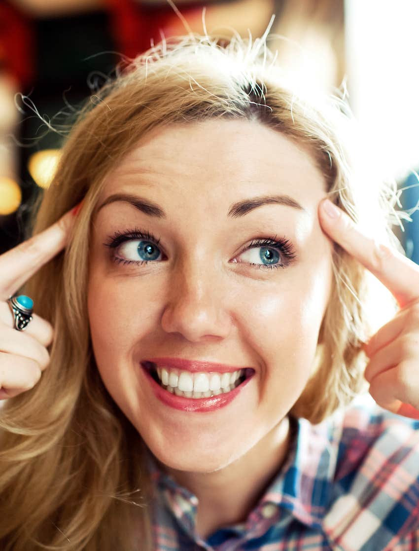 Woman points to either side of her head and smiles