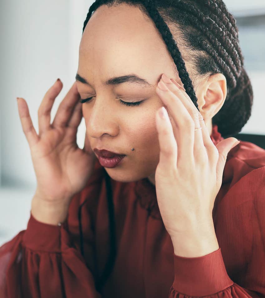 Woman holds fingers to temples of head with eye closed