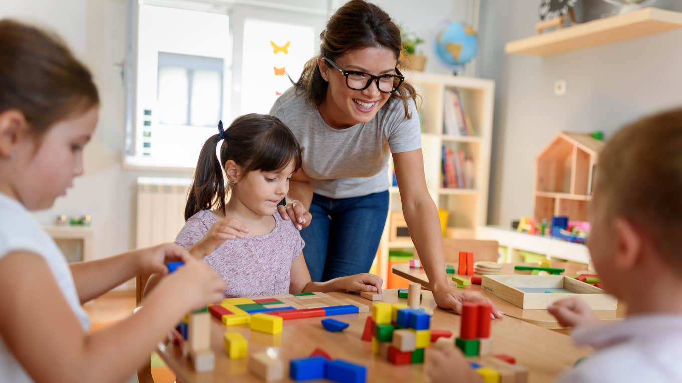 Preschool teacher with children playing with colorful wooden toys at kindergarten