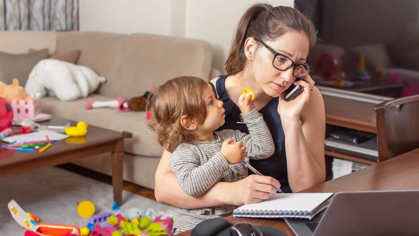 woman holding baby talking on mobile phone and working on a laptop