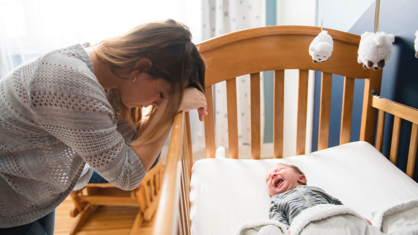 sad, tired mother leaning on her baby's crib