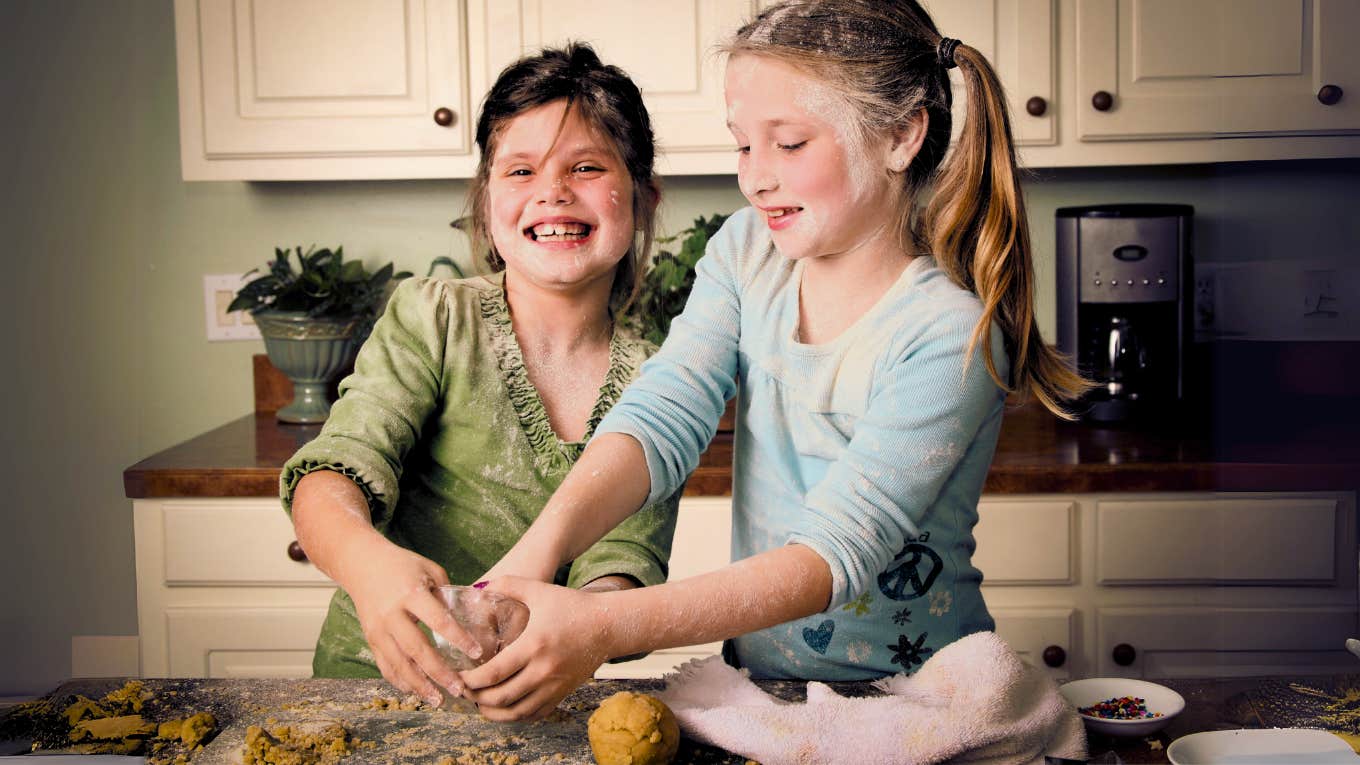 Mother taking hands off 1980's parenting approach while children bake in kitchen making a mess. 