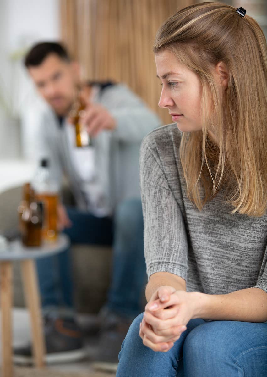 she hold hands and arms close while he gestures with a bottle in background