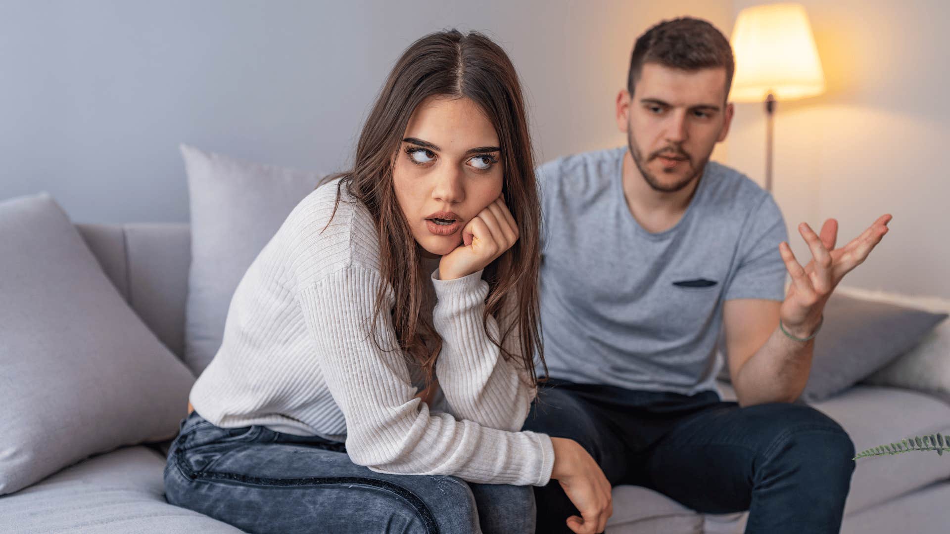 Unhappy couple quarreling, sitting apart indoors.