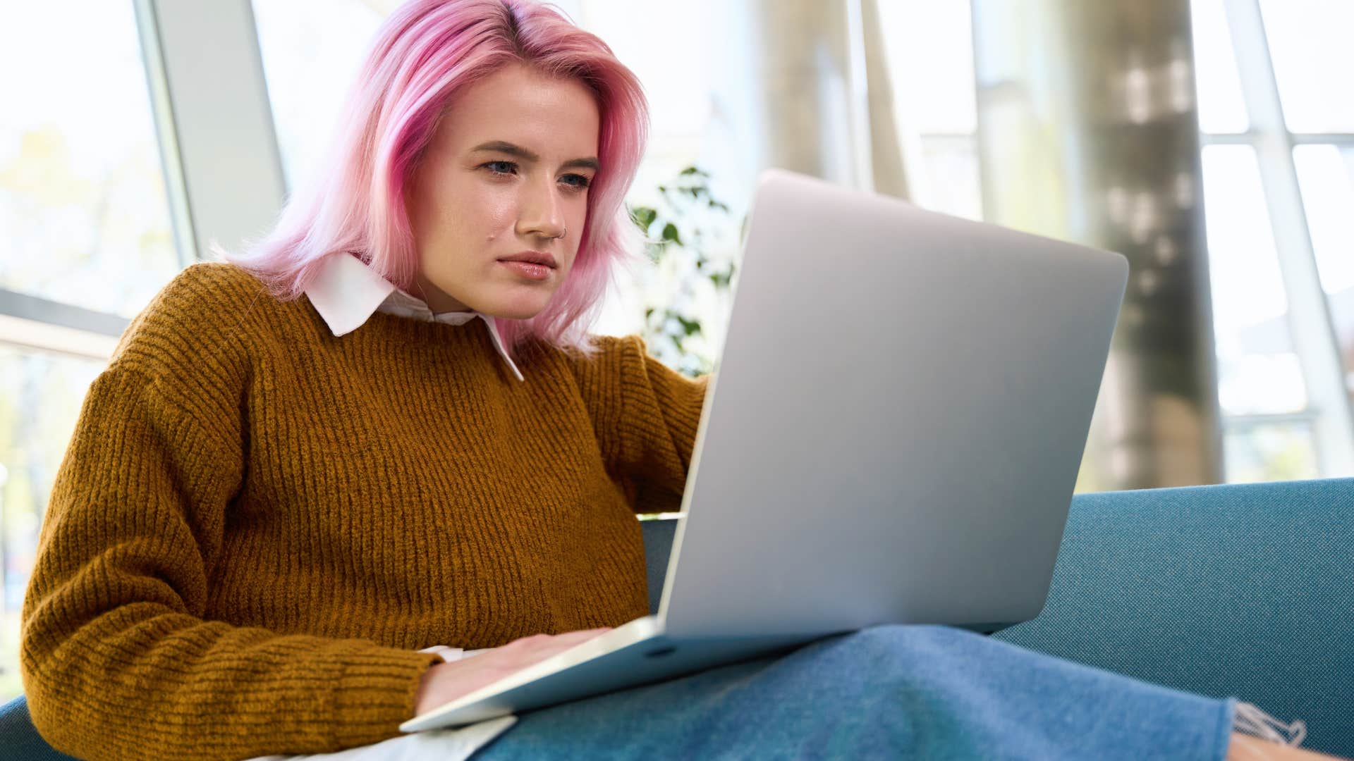 Woman with pink hair looking confused staring at her laptop. 