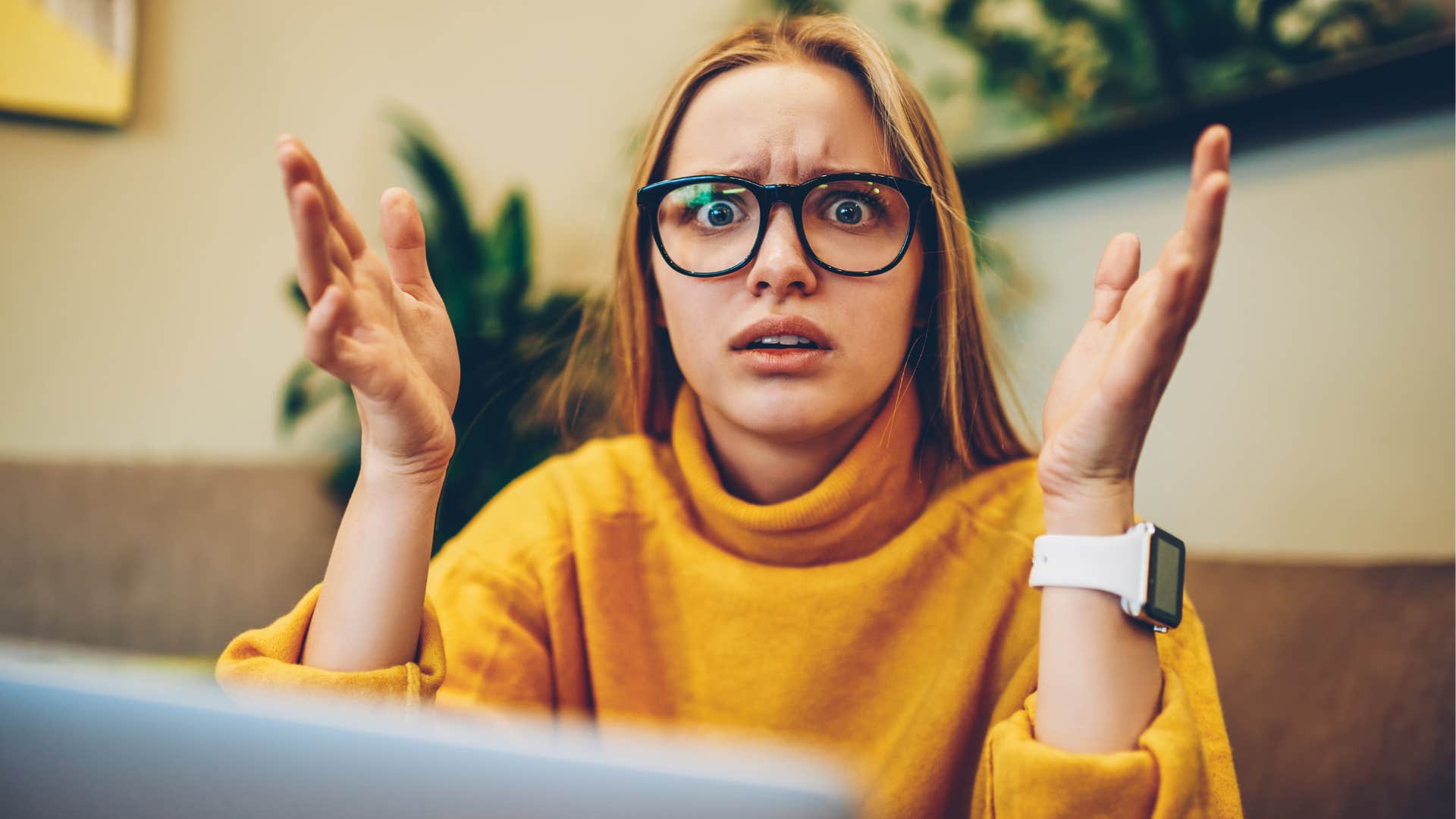 Woman wearing glasses looking confused at her desk.