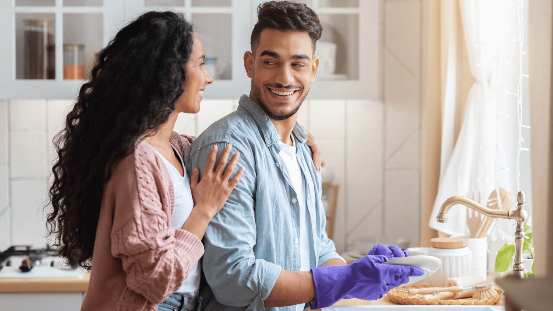 woman hugging man as he washes dishes