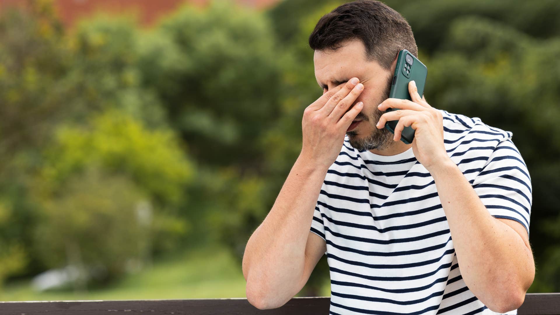 Man looking sad on the phone outside.