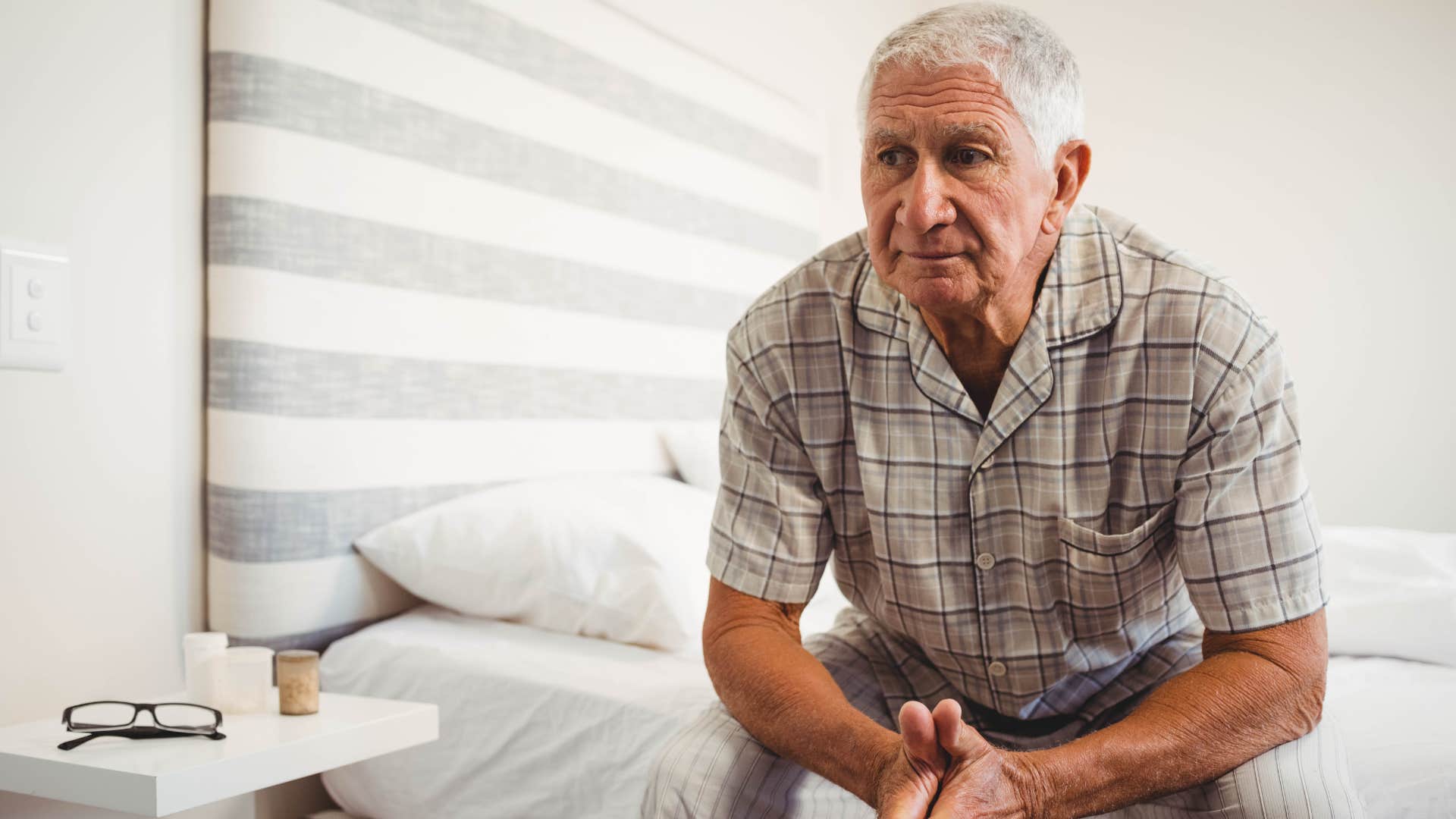 Older man looking upset on his bed.