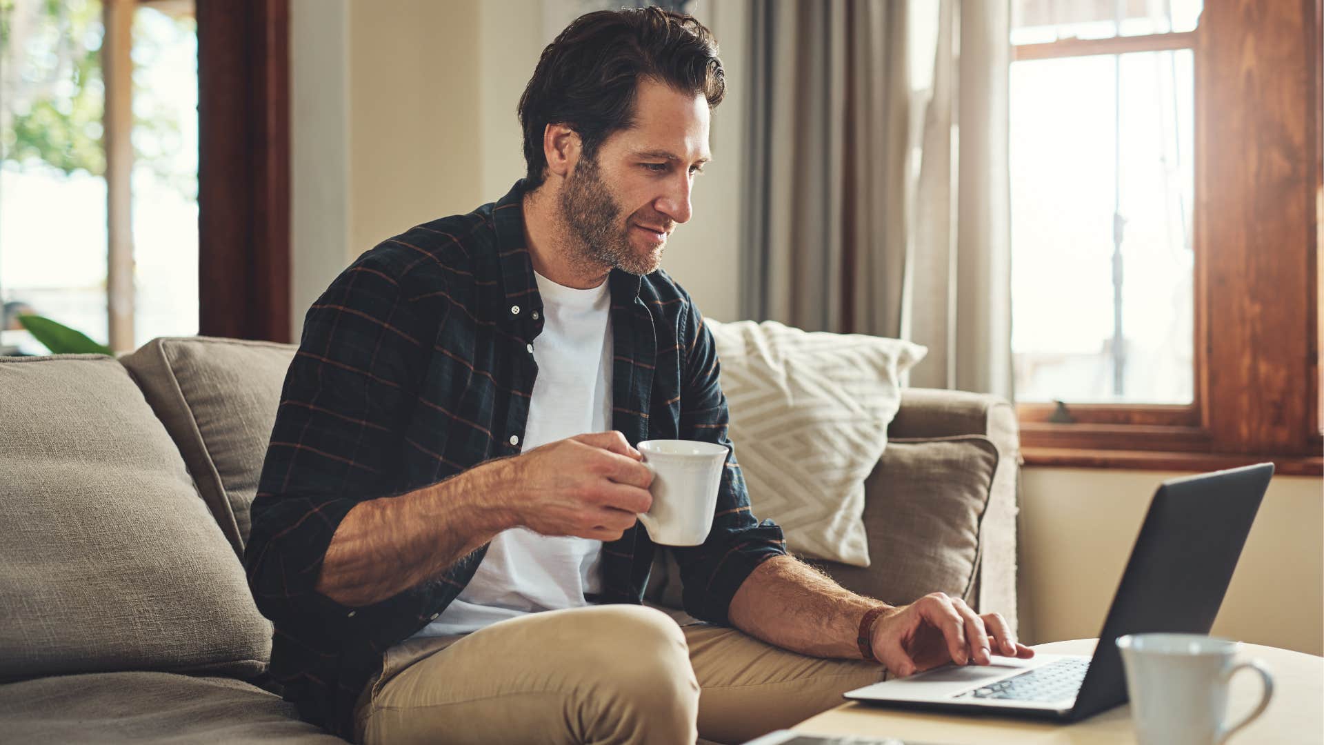 Man happily working on his laptop in the living room.