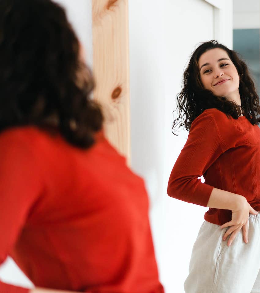 Woman in red sweater checks her outfit in the mirror