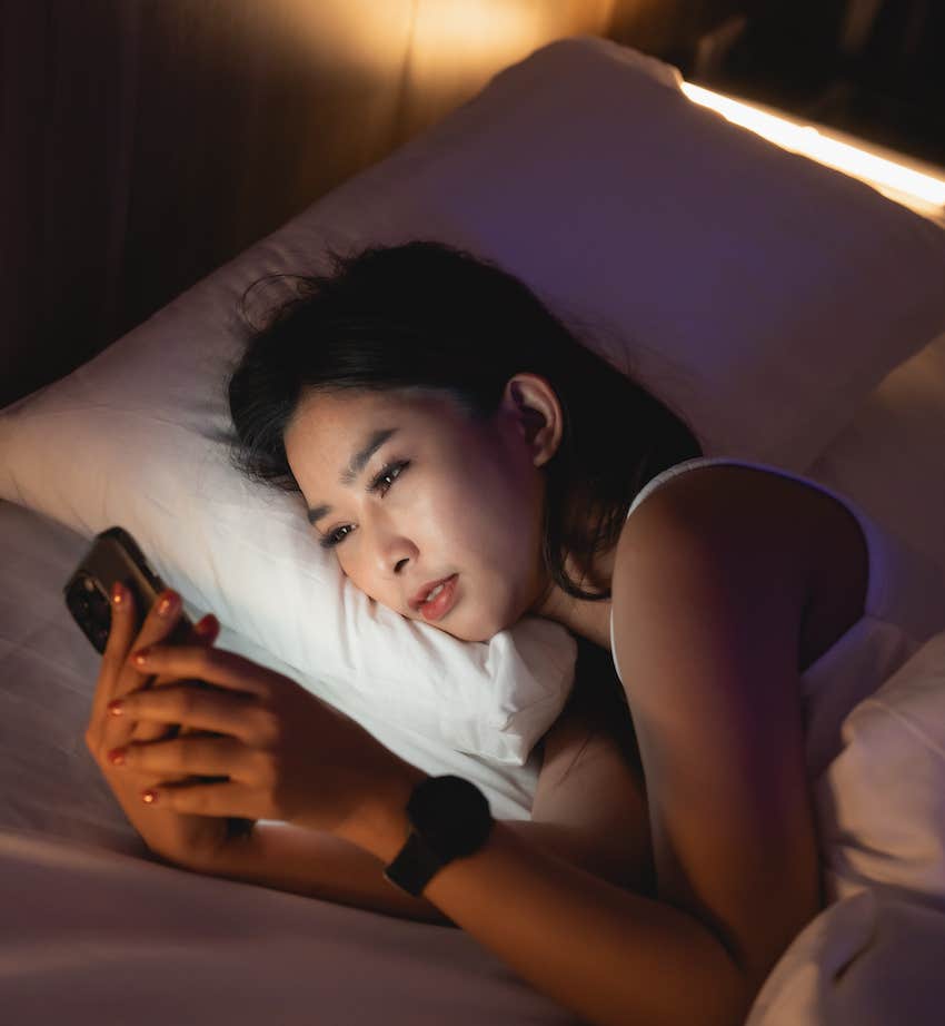 WOman lays in bed looking at mobile device