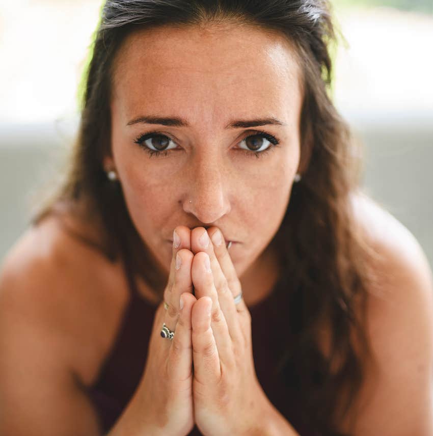 She holds hands palm-to-palm and looks intently into the camera