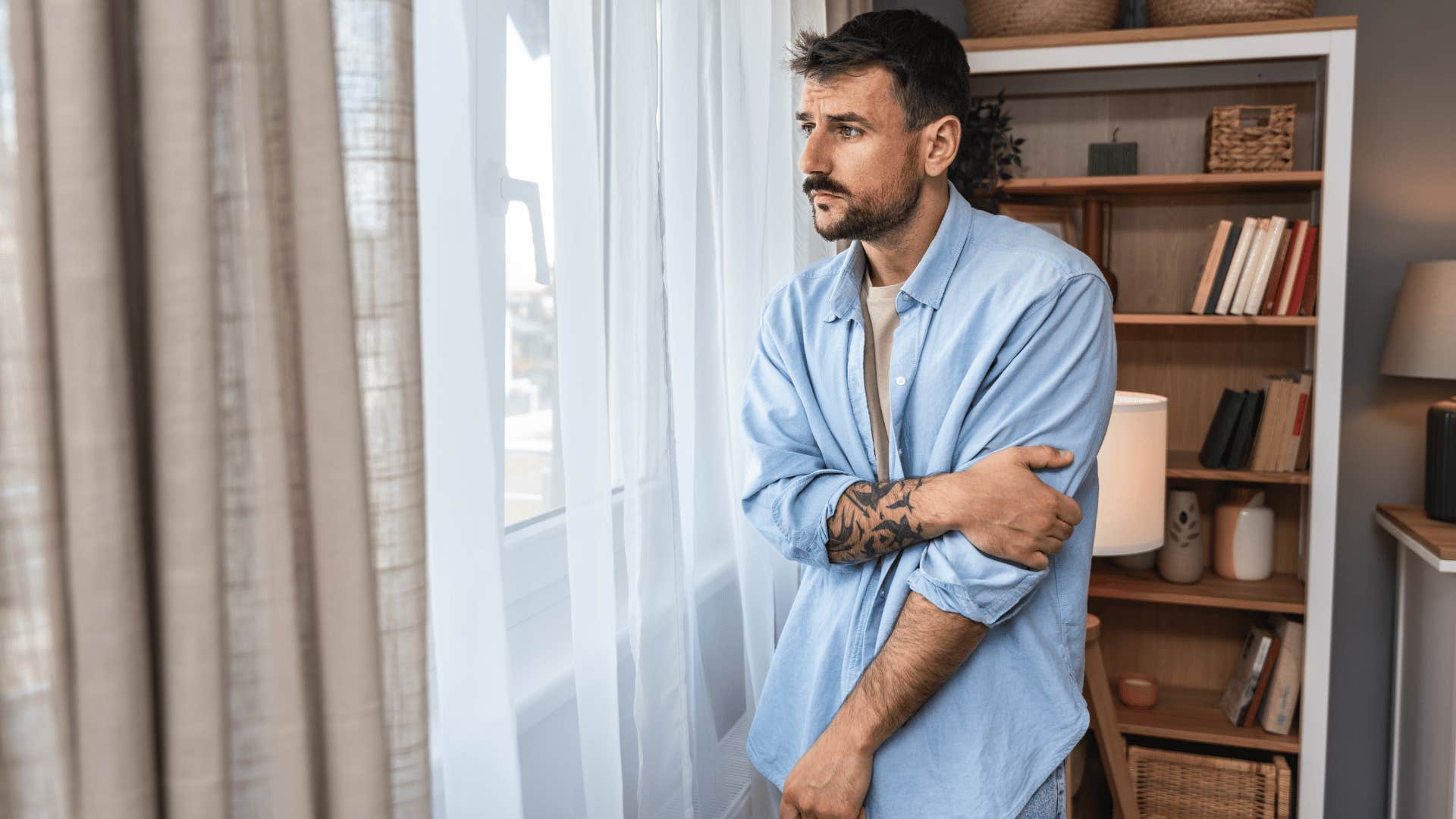 man looking out window looking depressed