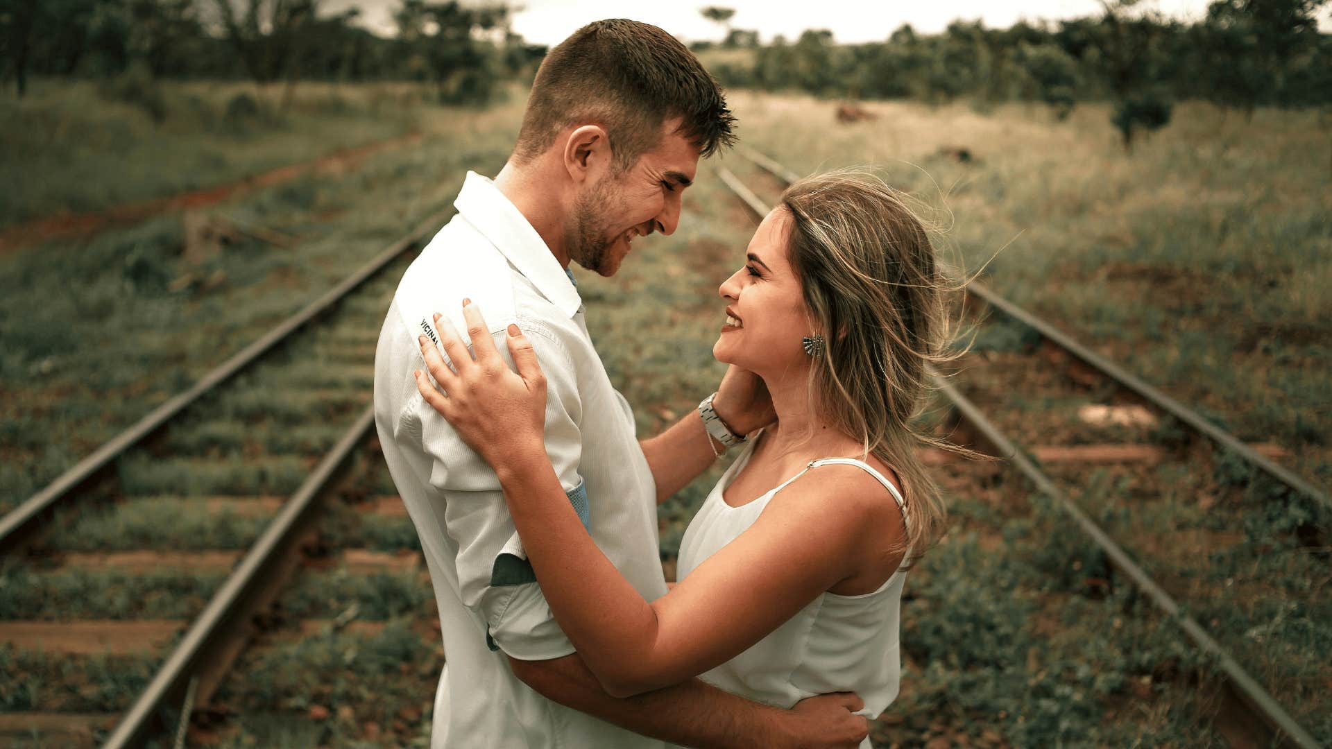 smiling couple holding each other on railroad tracks